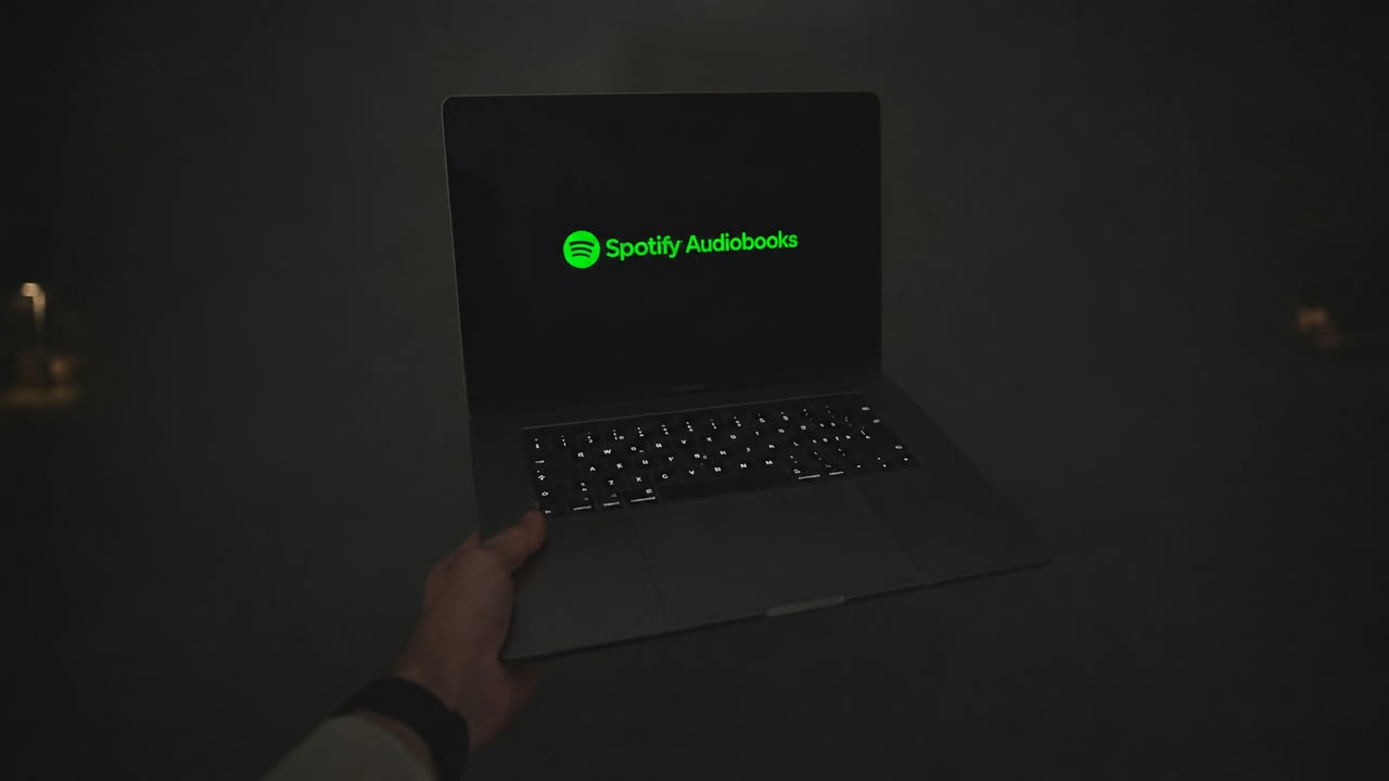 A person holding a laptop in a dark room showing the Spotify logo on the screen.