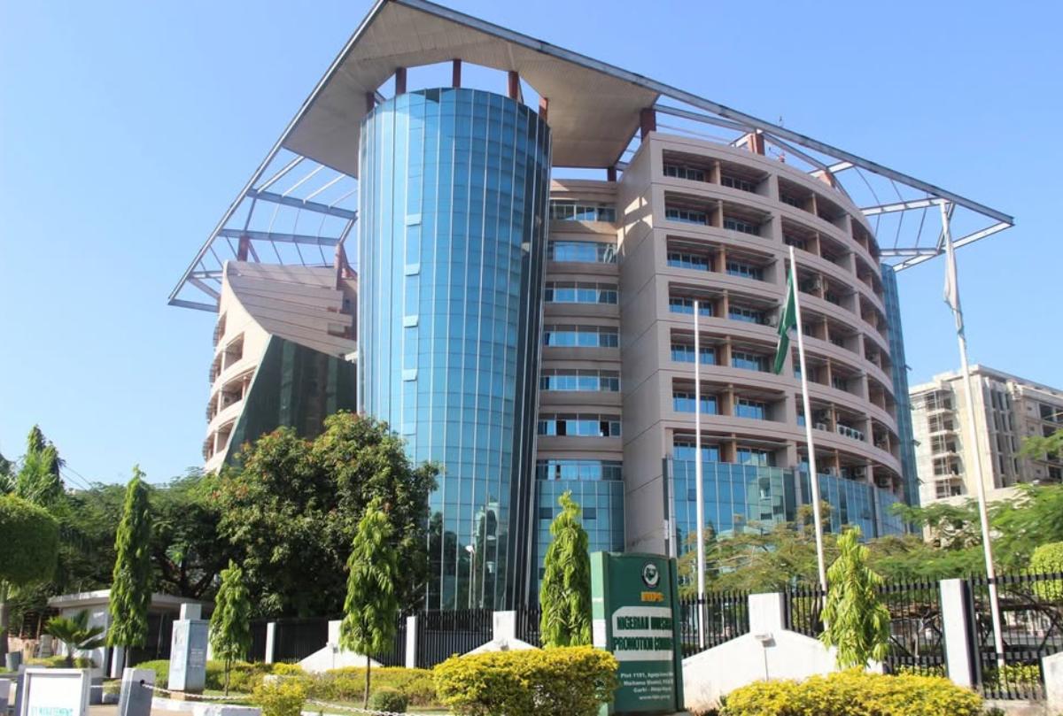 Exterior view of the Nigerian Communications Commission (NCC) headquarters in Abuja, featuring a curved glass tower, modern office building and Nigerian flag.